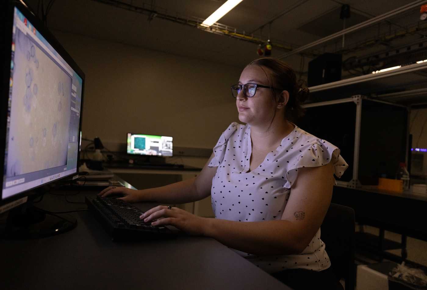 A female student works in a lab with lasers looking at images of cells, reflecting hands-on research in the BS in Biophysics.