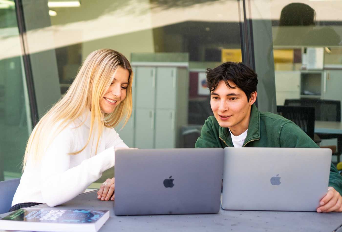 Two neuroscience students collaborate on laptops at an outdoor campus table, demonstrating collaborative learning in the minor in Neuroscience.