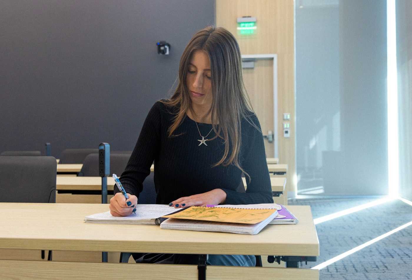 A female student sits at a desk and writes notes in a notebook, exploring living systems in ASU's Biological Sciences, BS program.