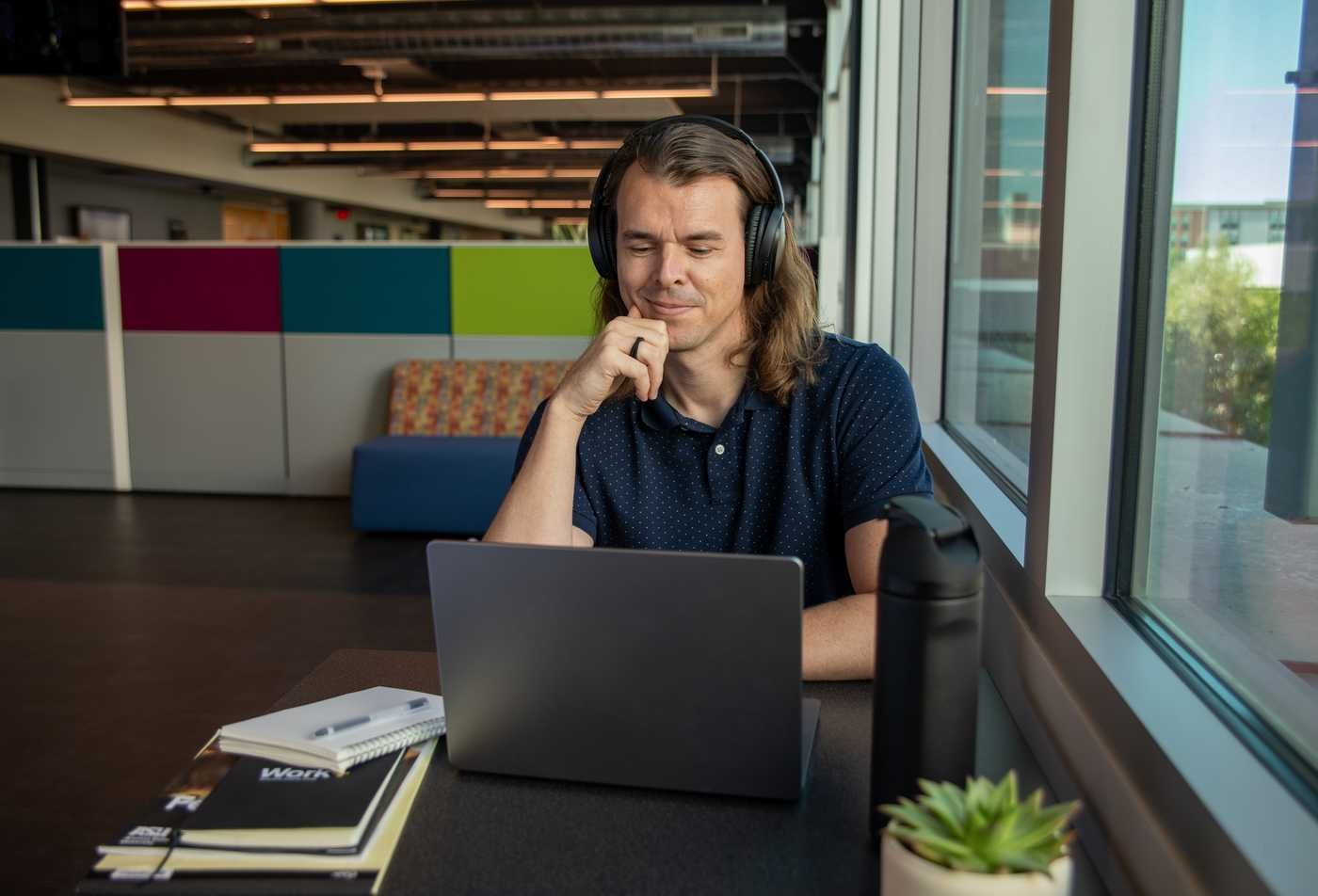 A male student sits in front of a laptop with headphones on, showcasing field explored in the Computer-Assisted Language Learning (Graduate Certificate).