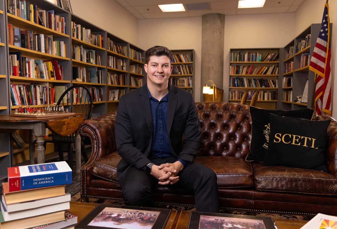 Alex England, a School of Civic and Economic Thought and Leadership student smiles, posing in the School of Civic and Economic Thought and Leadership library.