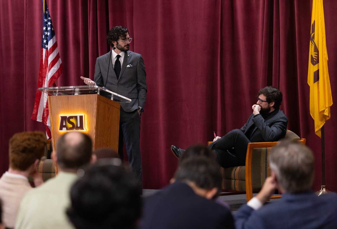 A speaker addresses an audience beside U.S. and ASU flags, reflecting civic dialogue in ASU's Civic and Economic Thought and Leadership, BS program.