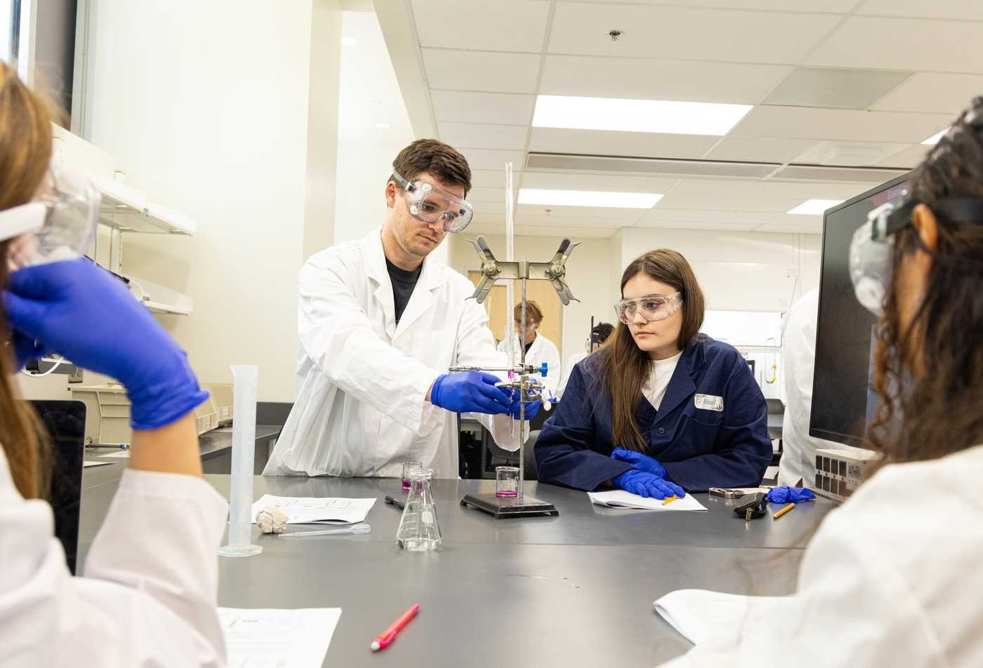 Four students perform a chemistry experiement together, showcasing collaborative learning in the minor in Chemistry.