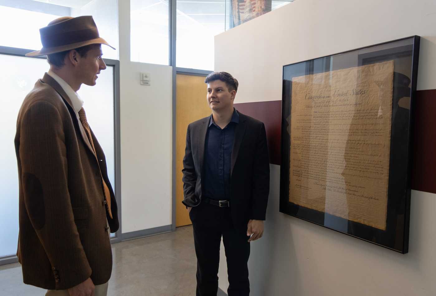 A student speaks with a professor in the hallway in front of framed American document, reflecting civic dialogue in the MA in Classical Liberal Education and Civic Leadership.