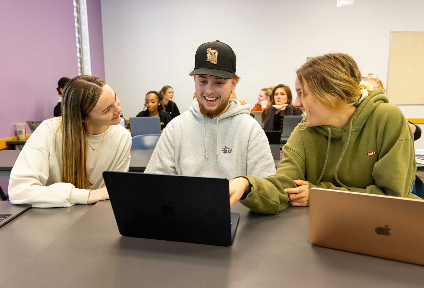 Three students smile while collaborating on a project on a computer, showcasing teamwork in the MA in Communication.