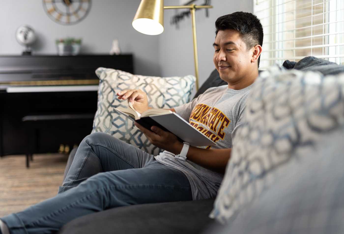 A student sits on a couch in a living room with a book in hand, showcasing flexible learning in the certificate in Critical Theory.