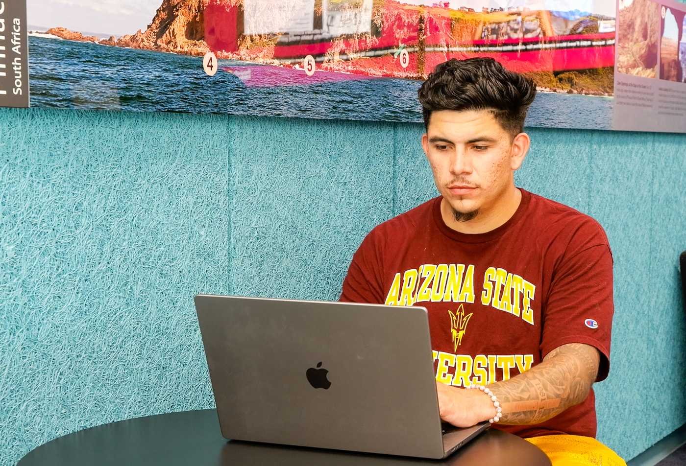 A student works on a laptop near a cultural display, exploring society in ASU's Culture, Technology and Environment, BA program.