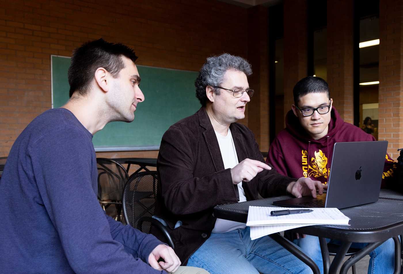 Two students sit with a faculty member, examining a laptop, building knowledge in the minor of Data Science.