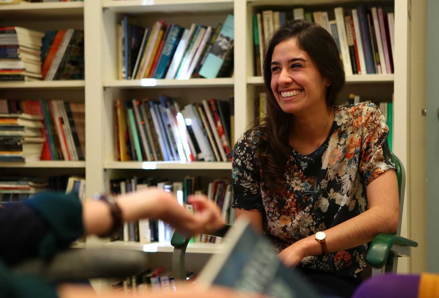 A female English graduate sits in front of a filled bookcase and smiles, developing communication skills in the English, MA.