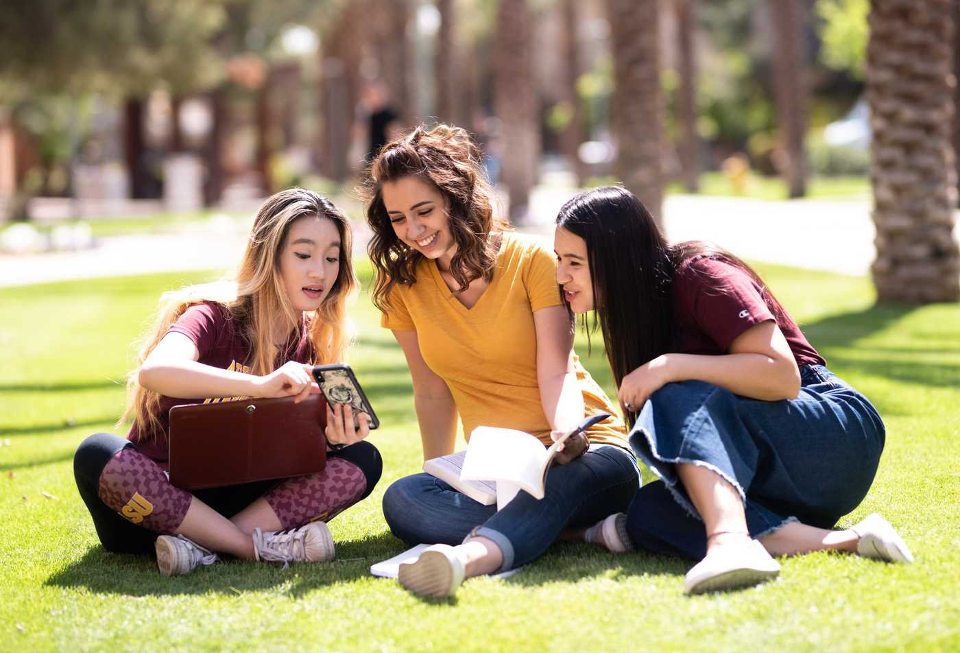 Three female students sit in grass reading together, showcasing the community in the minor in English - Literature.