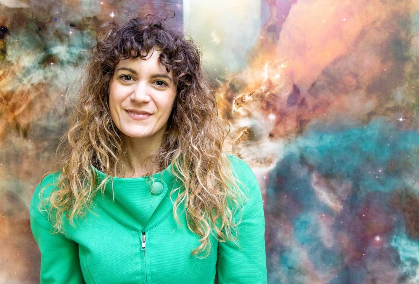 A student smiles into the camera while standing against a galaxy background, symbolizing the field explored in the Exploration Systems Design, PhD.