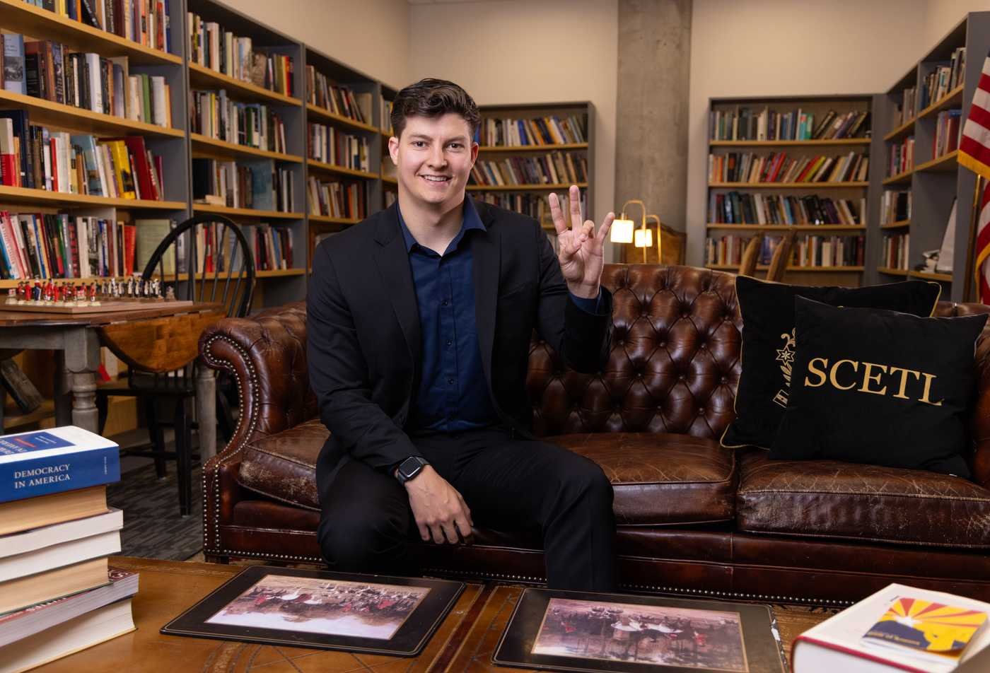 A student in a blazer sits on a leather sofa in a  School of Civic and Economic Thought and Leadership library setting, showcasing the field explored in the certificate in Great Books in Political Thought