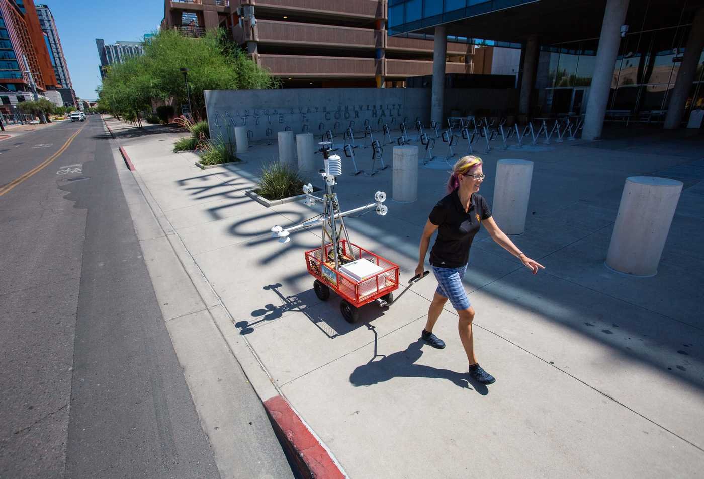A professor pulls a mobile weather station along a shaded sidewalk at ASU Coor Hall, showcasing the hands-on research accomplished in the Geography, PhD.