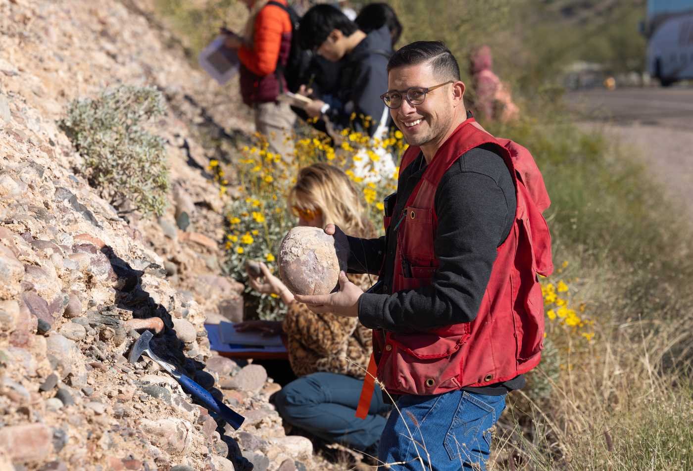 A student examines a rock during fieldwork, showcasing the topics explored in the Geological Sciences, MS.