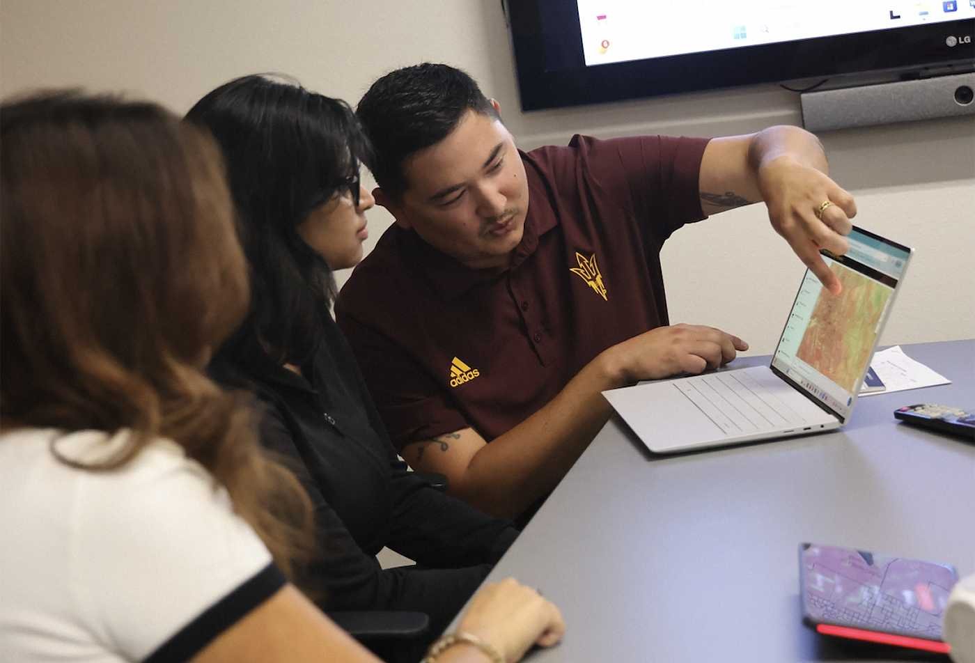 A professor shows students a digital map on a laptop during a small-group lesson, demonstrating collaborative learning in the certificate in Geographic Information Science.