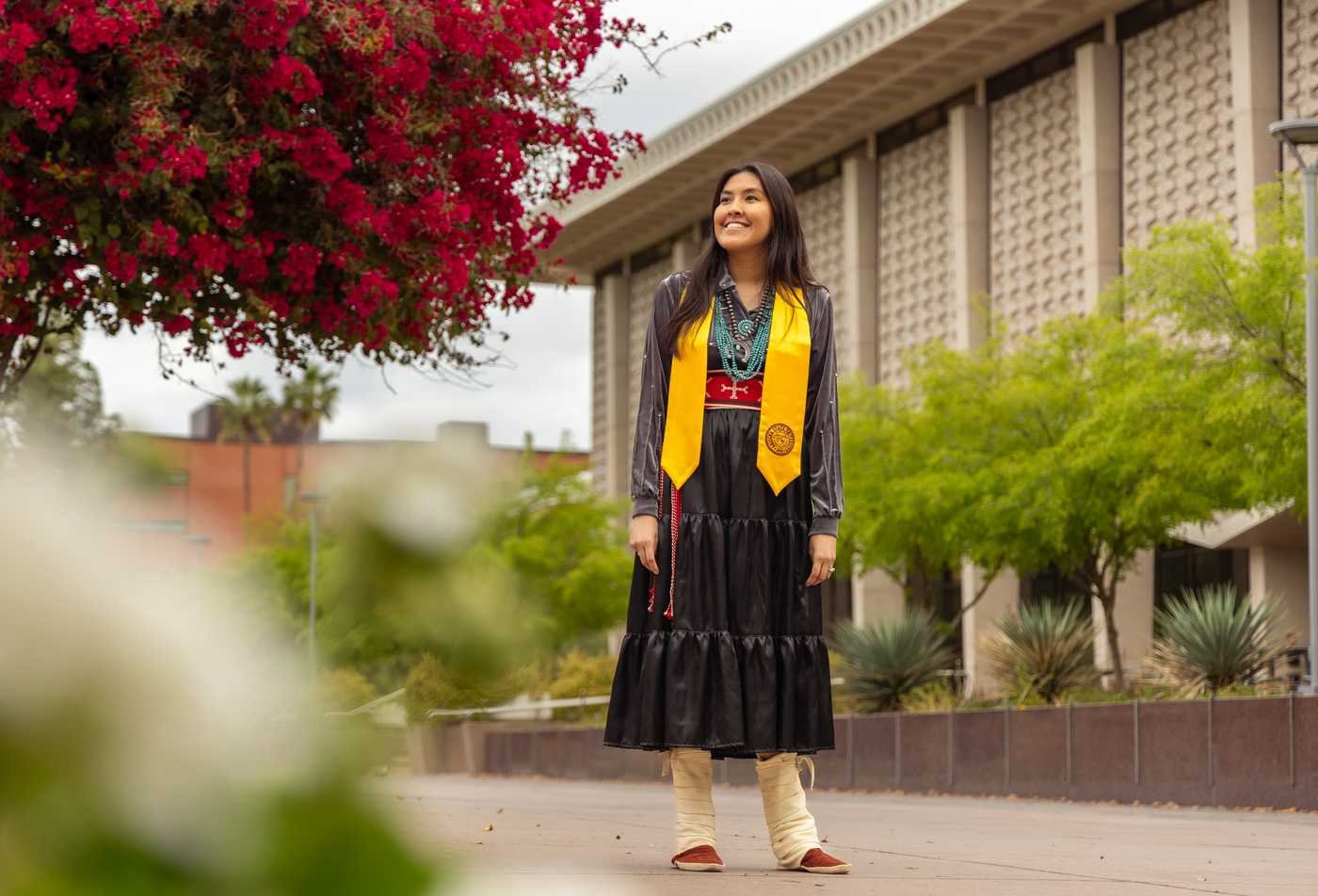 A female student wearing a traditional Indigneous outfit with the ASU graduation stole, showcasing her success in the Indigenous Education, MA.