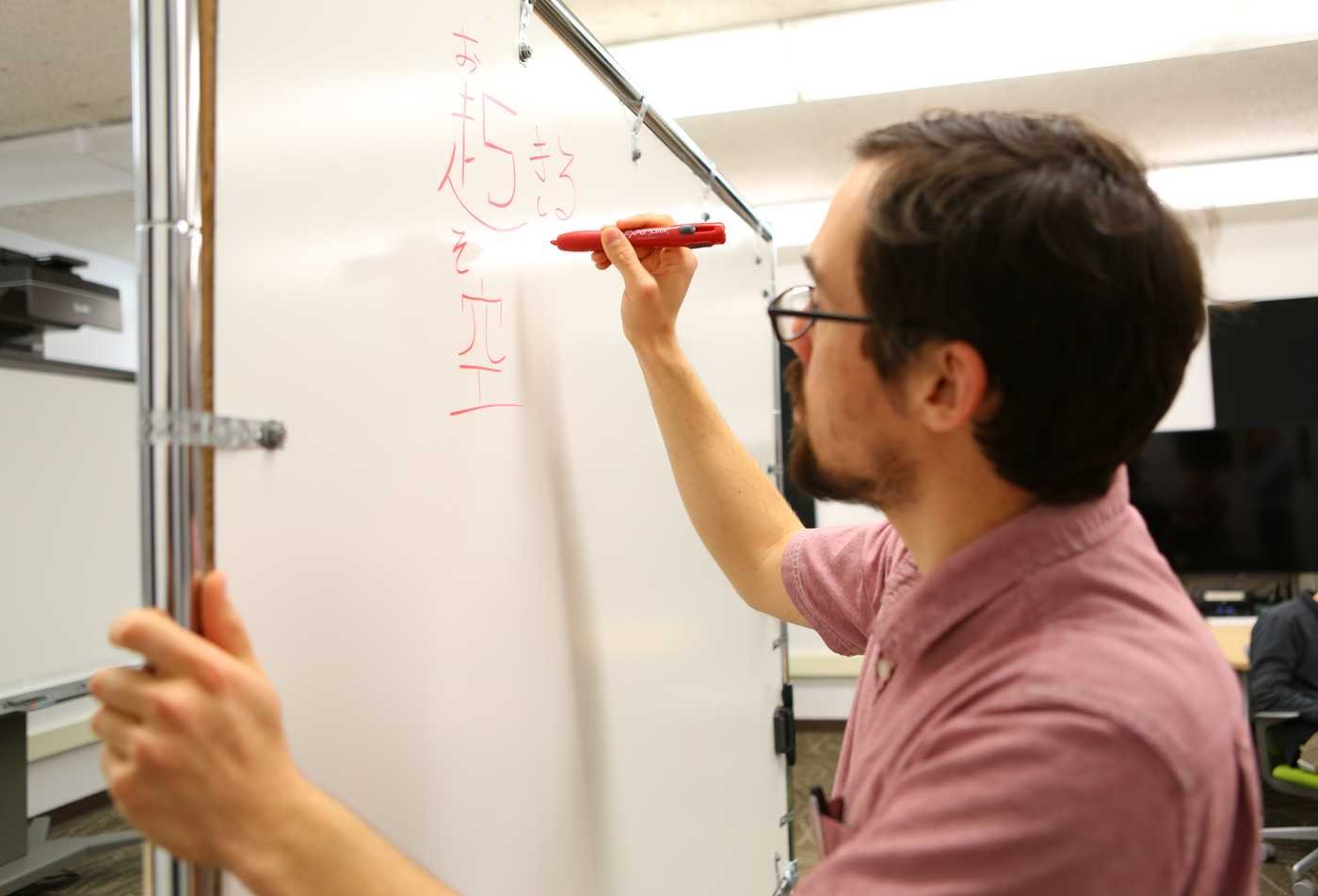 A male student writes japanese words on a whiteboard, demonstrating expertise gained in the minor in Asian Languages - Japanese.