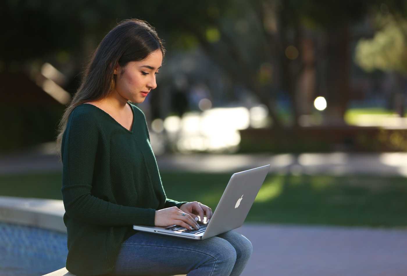A justice studies student studies on her laptop outside, developing her understanding of society in the MS in Justice Studies.