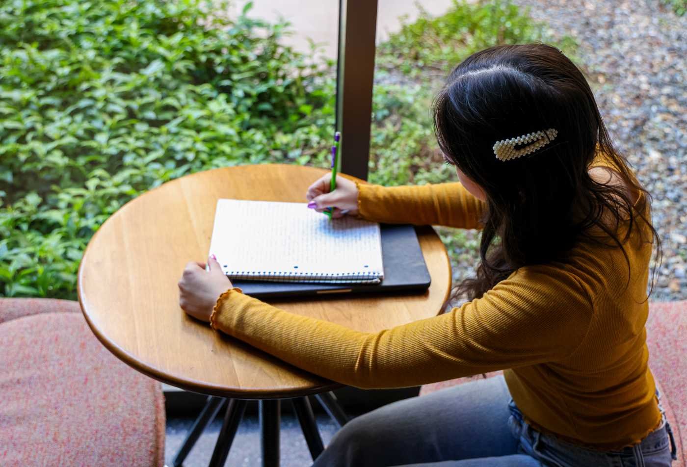 A student takes notes in a notebook on a table, studying as part of the Justice Studies, PhD.