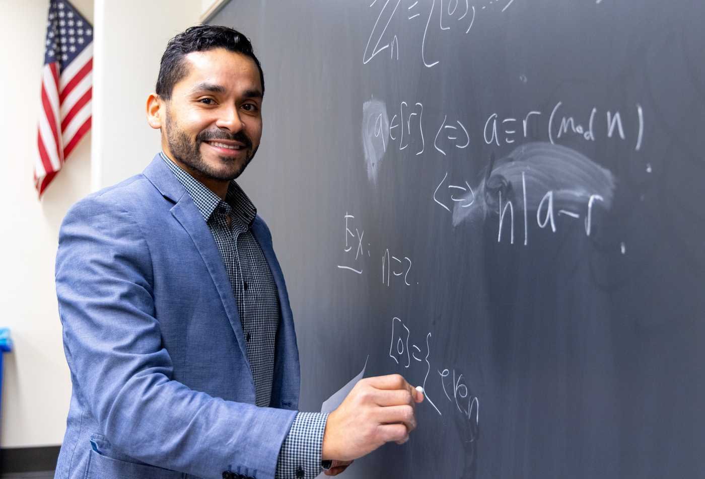 A professor writes equations on a blackboard, demonstrating field explored in the Mathematics, PhD.
