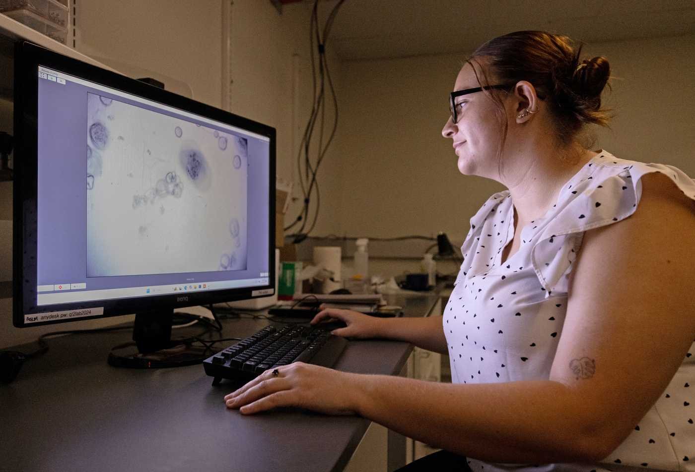 A female scientist analyzes a microscopic specimen on a computer in a dark room.