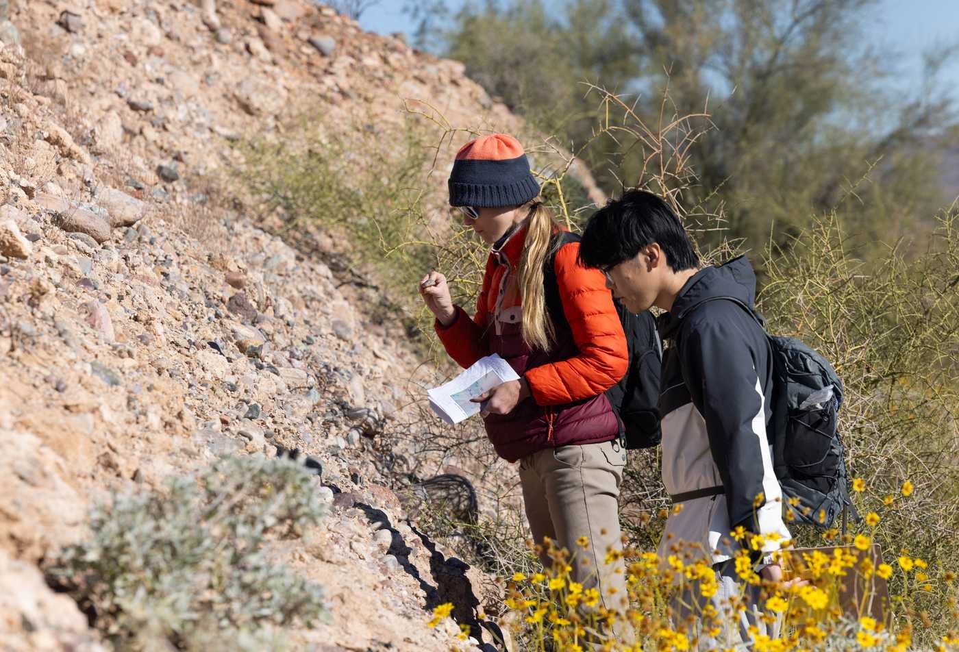 Two students examine a rocky desert hillside, demonstrating hands-on learning in the Natural Science (Earth and Space Sciences), MNS.