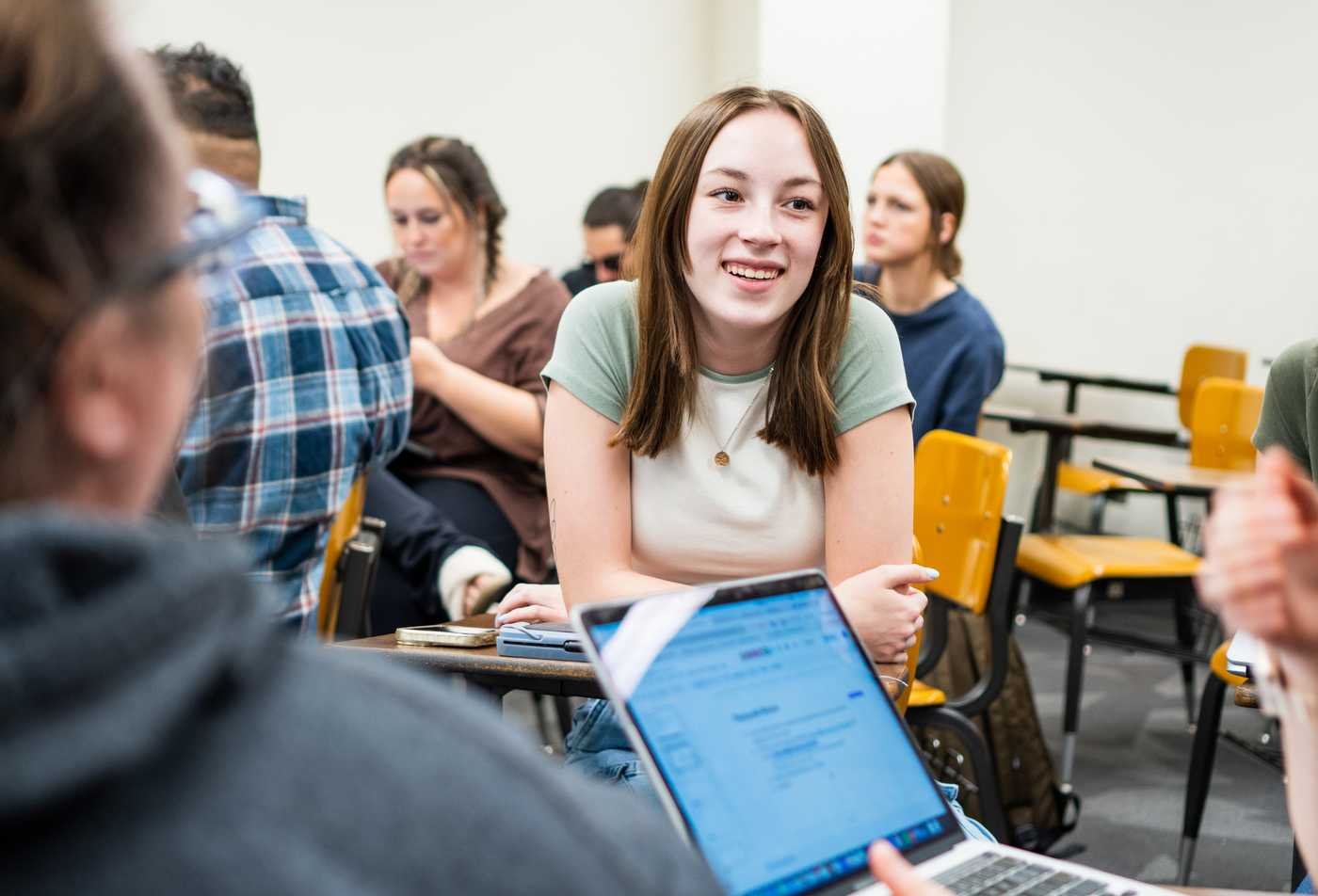 A student smiles and chats with classmates in a college classroom, demonstrating in the community in the Psychology minor.