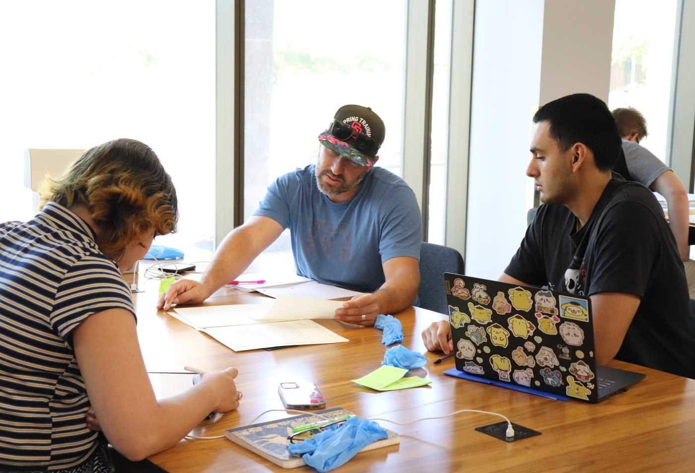Three students collaborate around a table, showcasing teamwork within the Public History (Graduate Certificate).