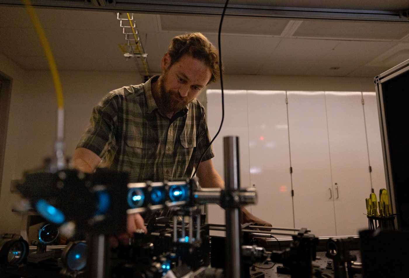 A researcher adjusts optical equipment in a dark lab, exploring light and matter in ASU's Physics, BA program.