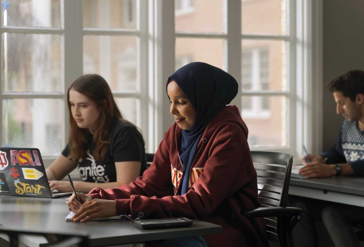 Three ASU students study in a bright classroom, connecting community and religion in the Religious Studies, MA.