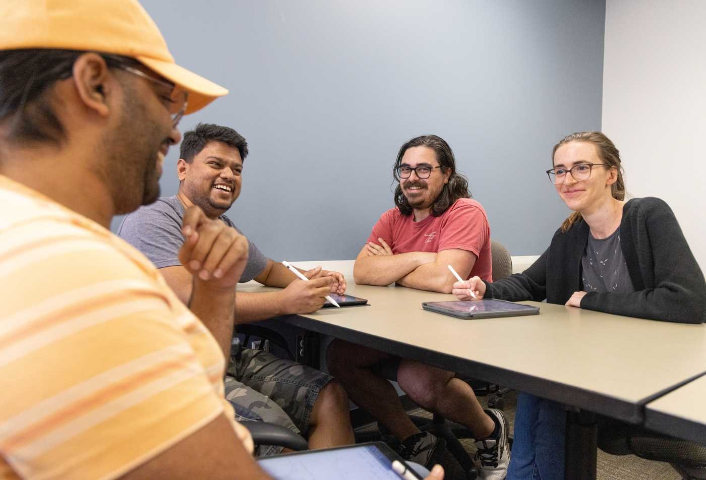 Four students laugh and engage in discussion around a table in a study room, showcasing collaboration in the Religious Studies, PhD.