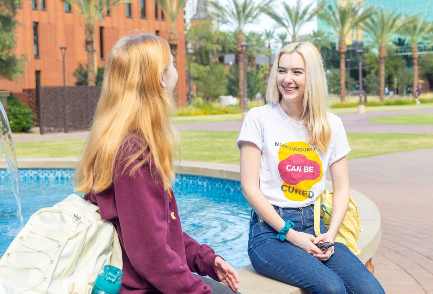 Two students talk by a campus fountain, exploring language and culture in ASU's International Letters and Cultures, BA program.