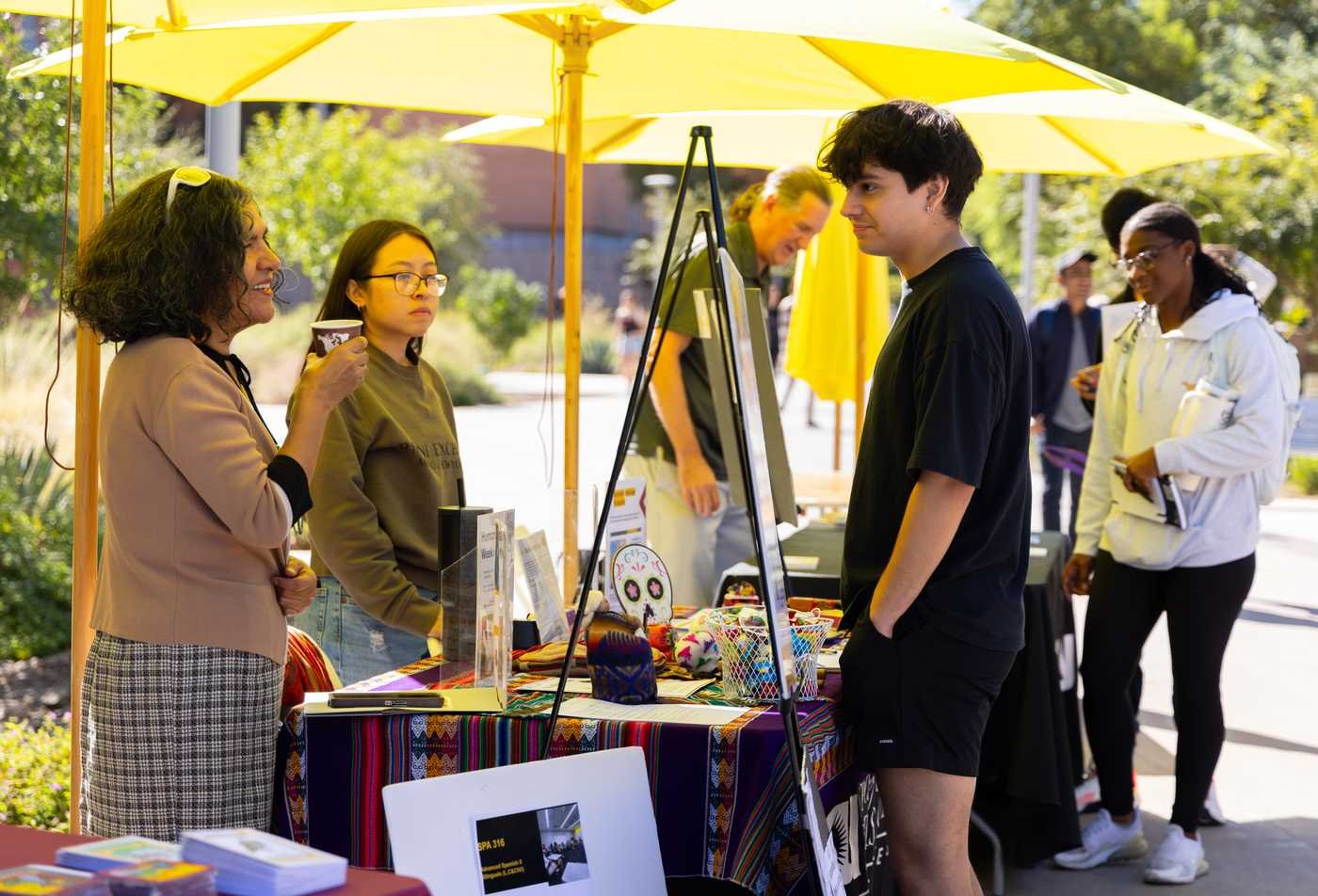 Students and staff chat around a table promoting Spanish language courses, showcasing the experience of the BA in Spanish.