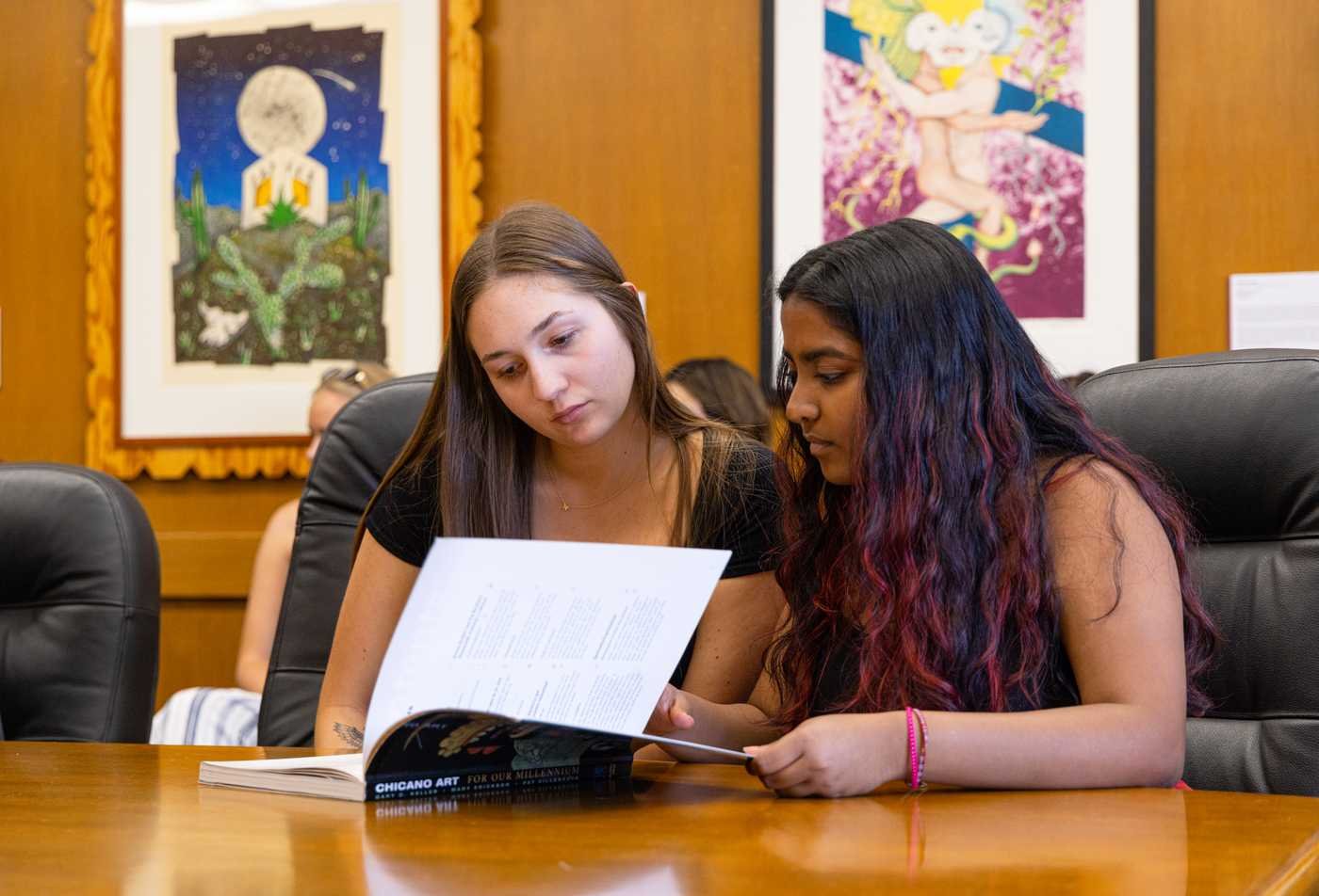 Students study a book of Chicano art, showcasing the field explored in Spanish Literature and Culture, PhD.