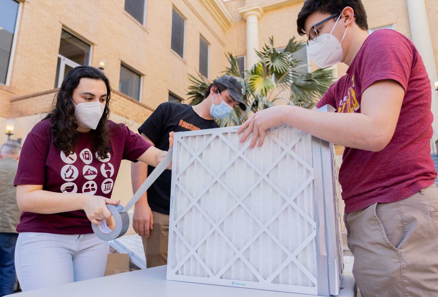 Three people work together to construct an air filter, demonstrating hands-on learning in the Global Health, MS.