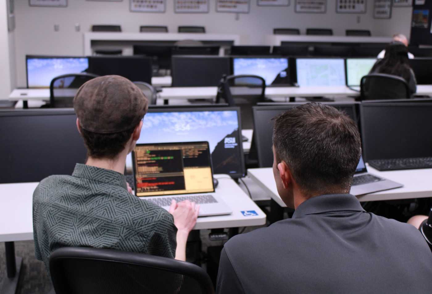 Student and professor work together on a laptop in a GIS computer lab, showcasing hands-on learning in the Social Science Research Methods (Graduate Certificate).