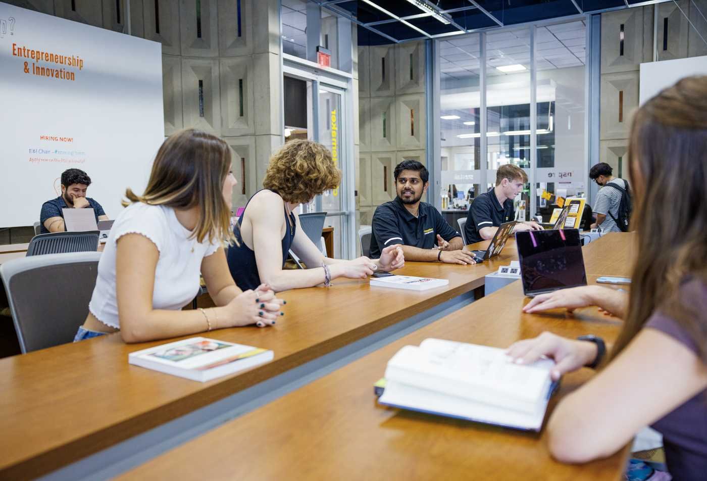 Colleagues in business casual attire have a conversation in a modern office common area, showcasing the field explored in Workplace Communication.