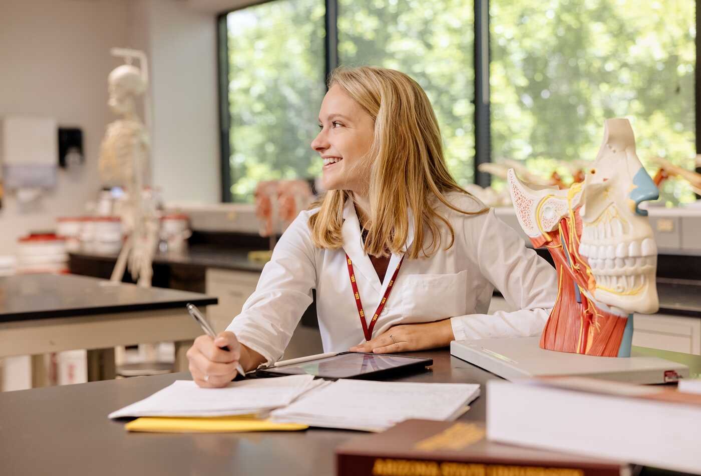 An anatomical head model sits beside a student studying in a biology lab, connecting coursework to ASU’s Applied Biological Sciences pre-dental program