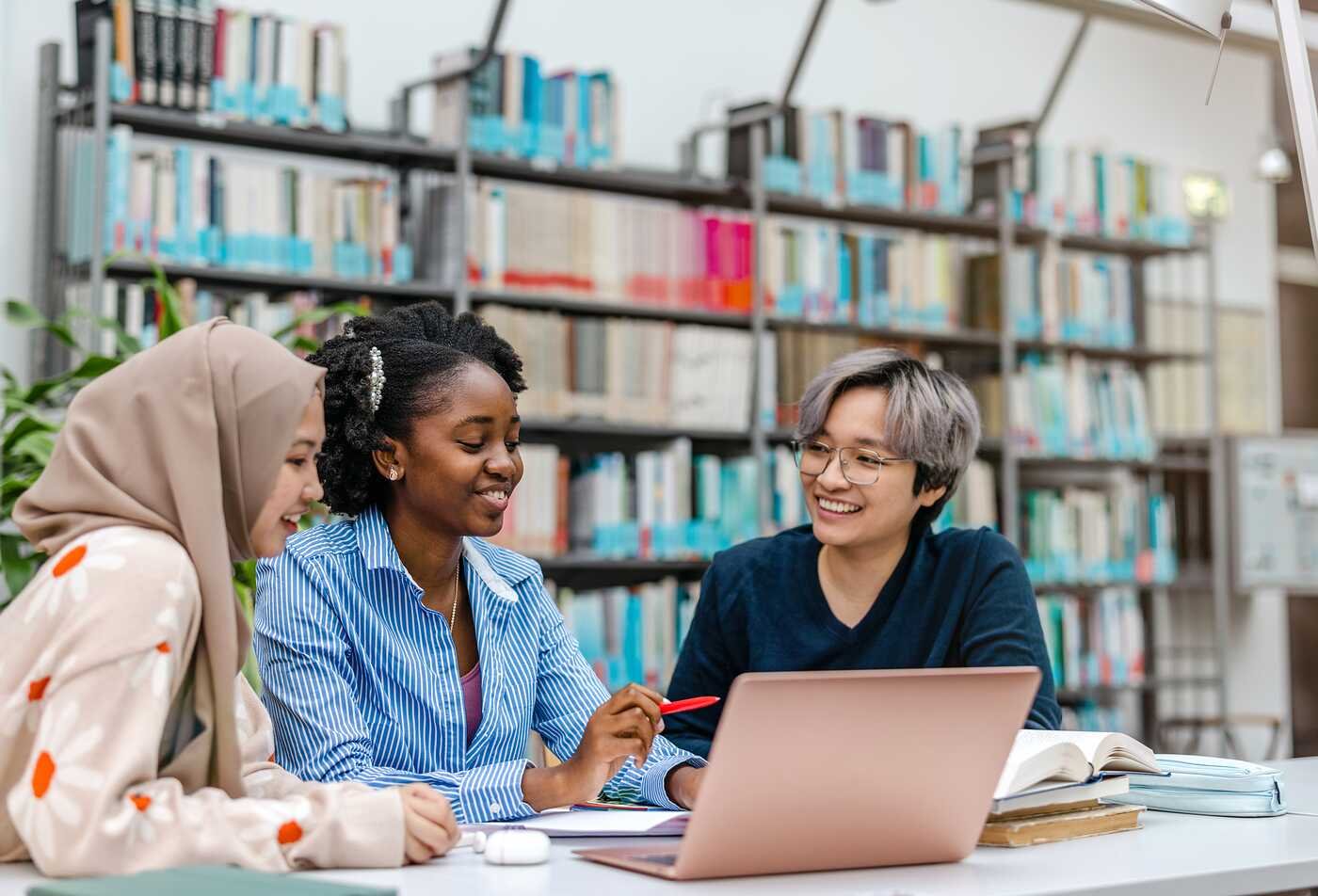 Around a library table, three students collaborate with a laptop, highlighting shared learning in ASU’s Communication program