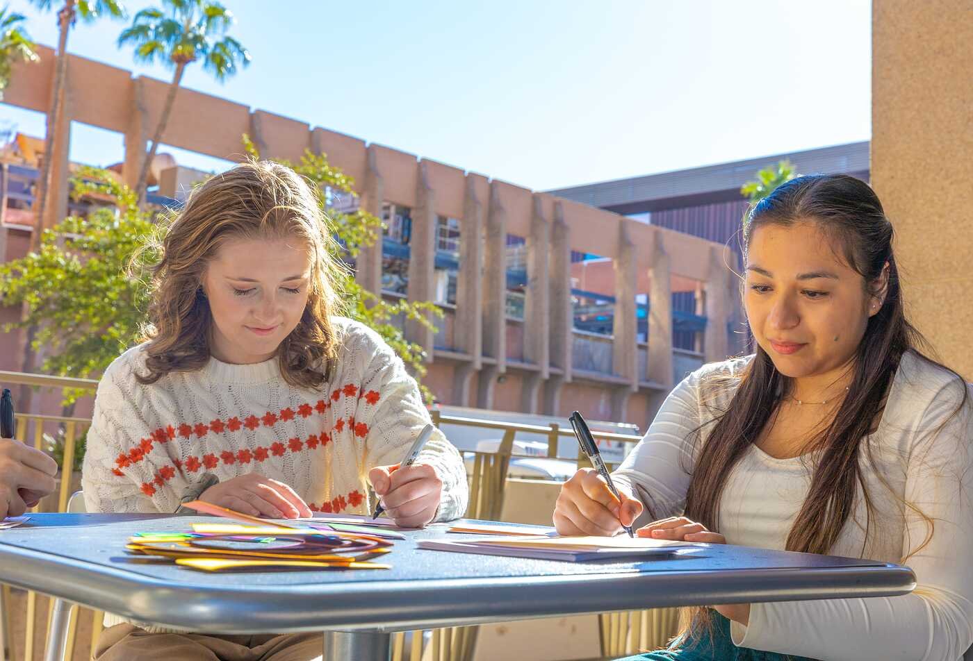 Two students write and collaborate outdoors, reflecting social inquiry in ASU's Integrative Social Science minor.