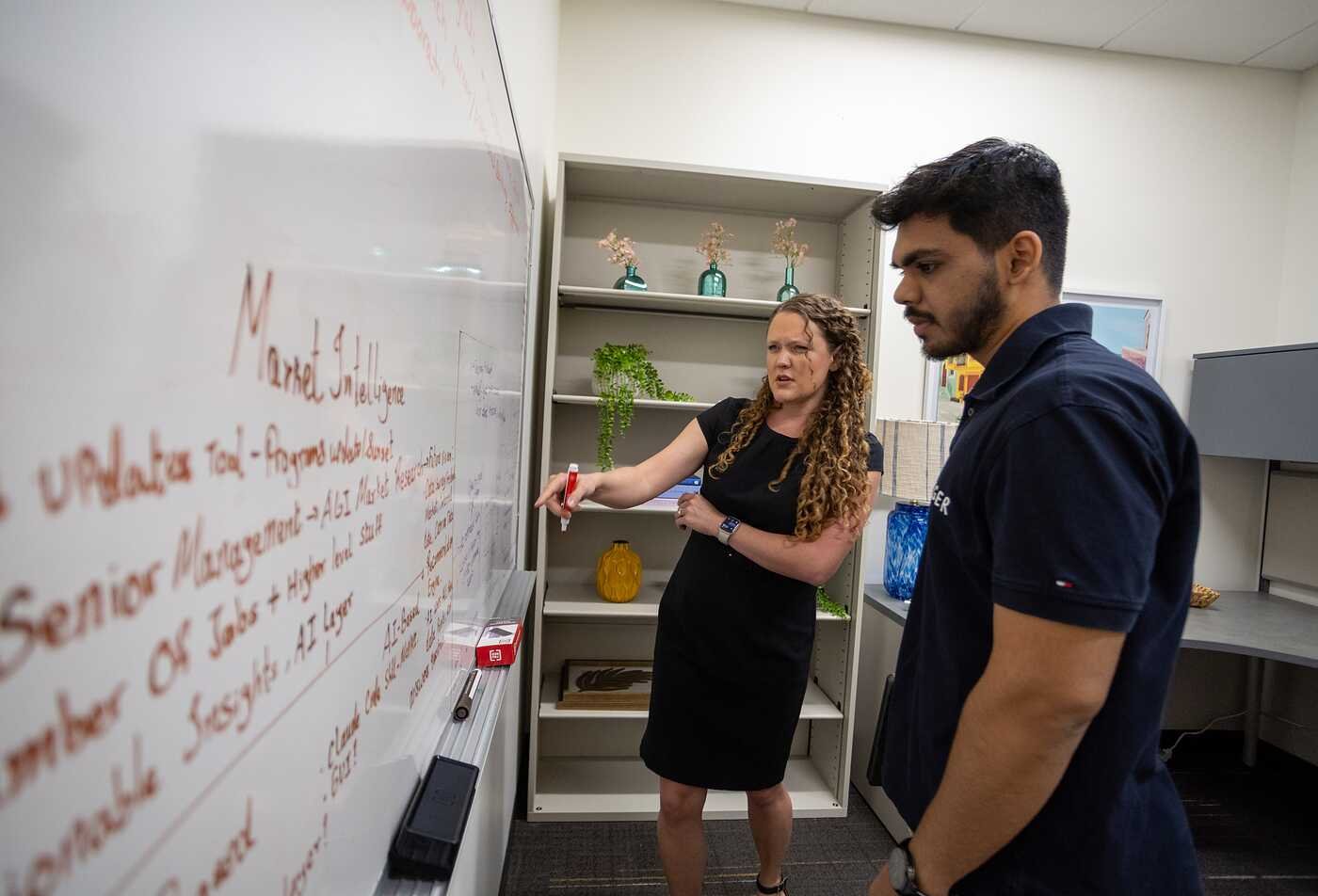 A mentor discusses organizational ideas at a whiteboard, building leadership skills in ASU's Organizational Leadership minor.