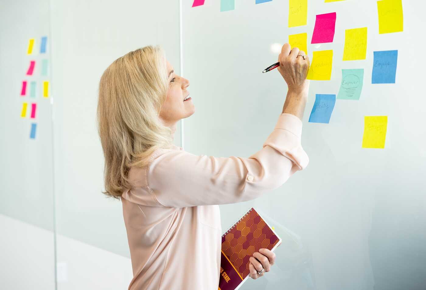 A professional organizes sticky notes on a board, developing planning skills in ASU's Project Management Essentials certificate.