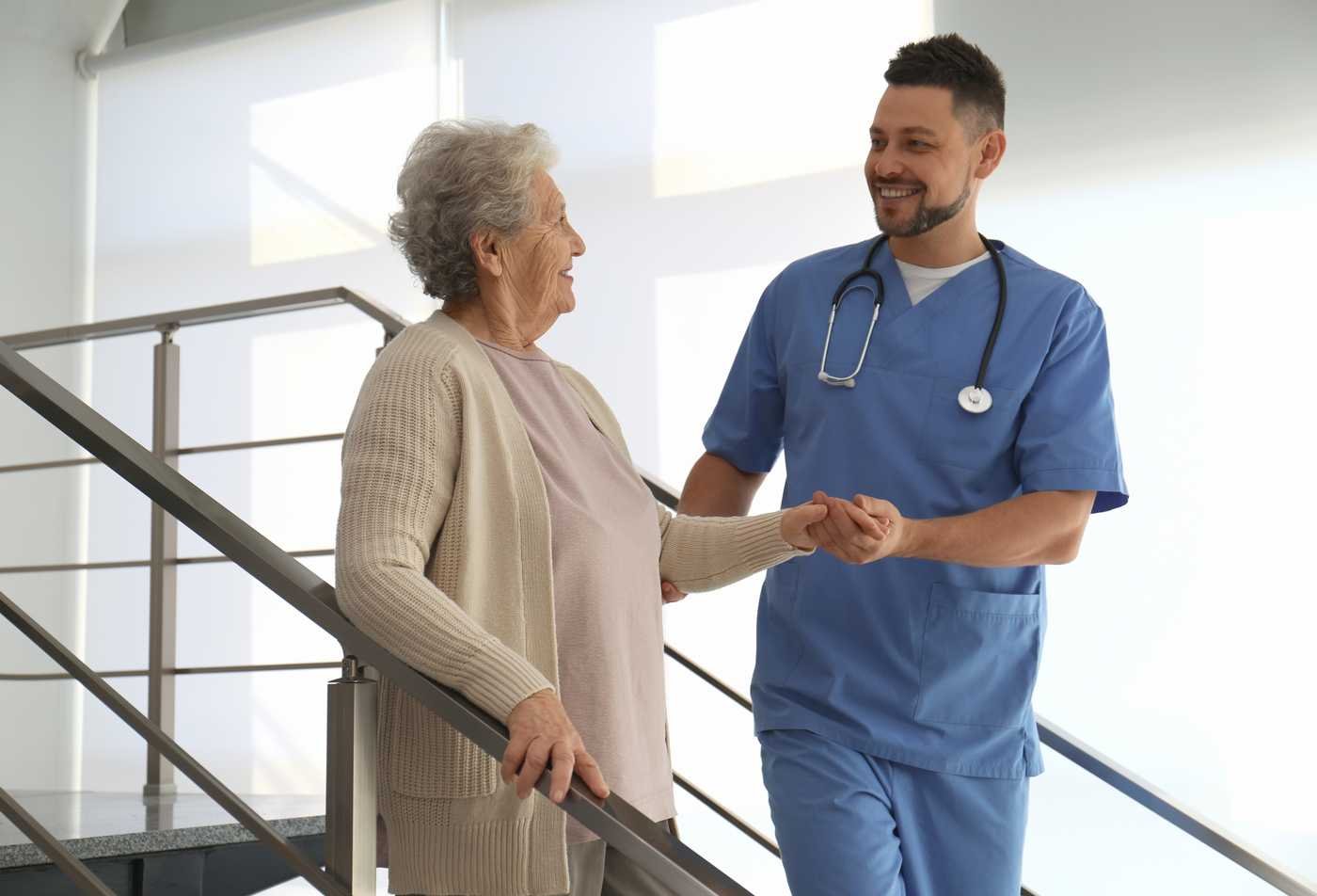 A DNP student assists an older adult patient with mobility during a clinical visit, symbolizing the field explored in the Advanced Nursing Practice (Adult-Gerontology Acute Care Nurse Practitioner).