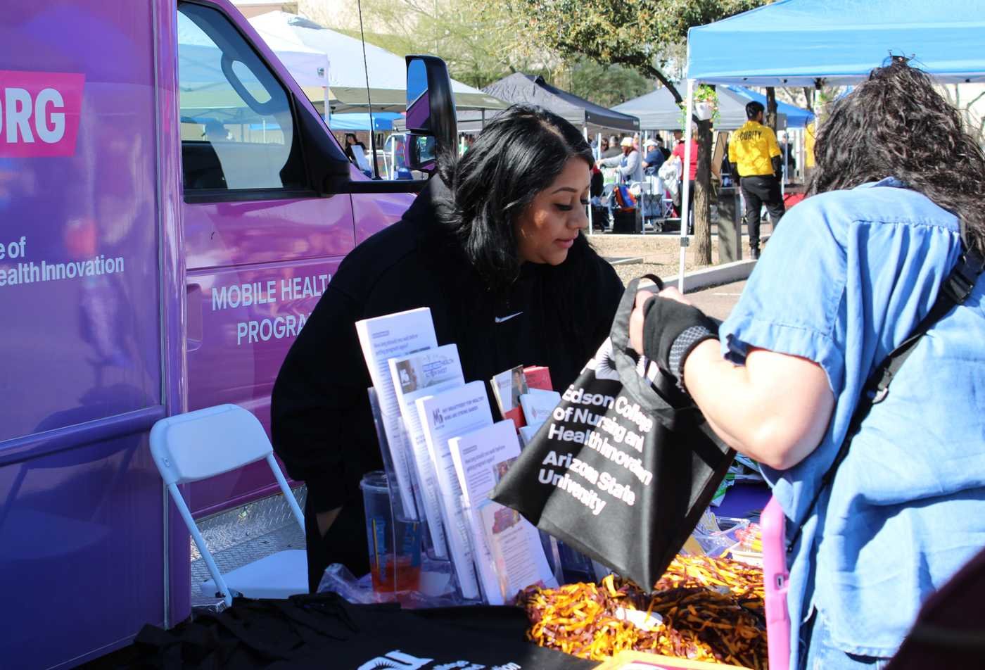 A student shares health resources with a community member at an outreach event, reflecting community connection in the BS in Community Health.