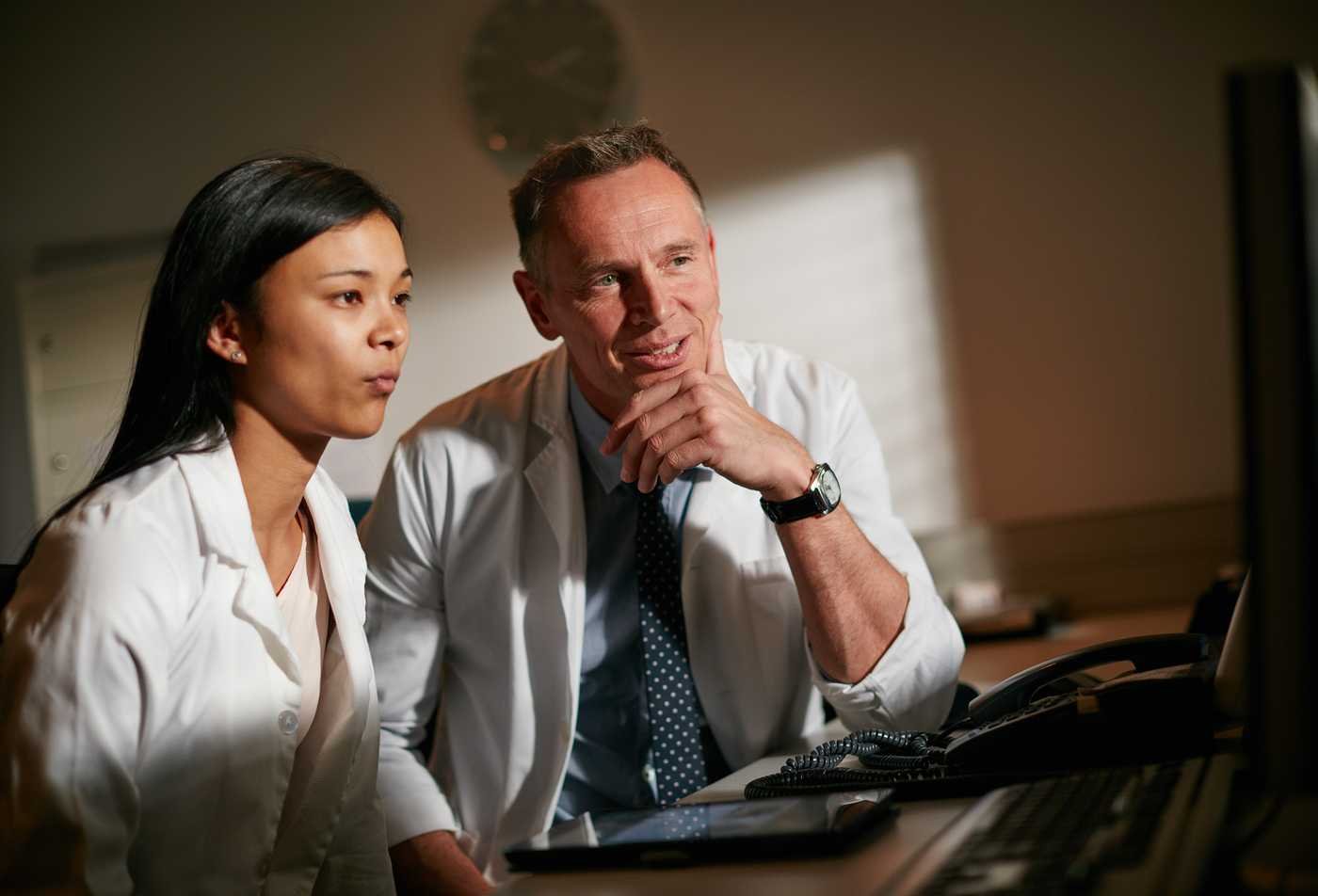 A student collaborates with a faculty member while reviewing health information on a computer, showing the collaborative learning environment of the BS in Health Care Compliance and Regulations.