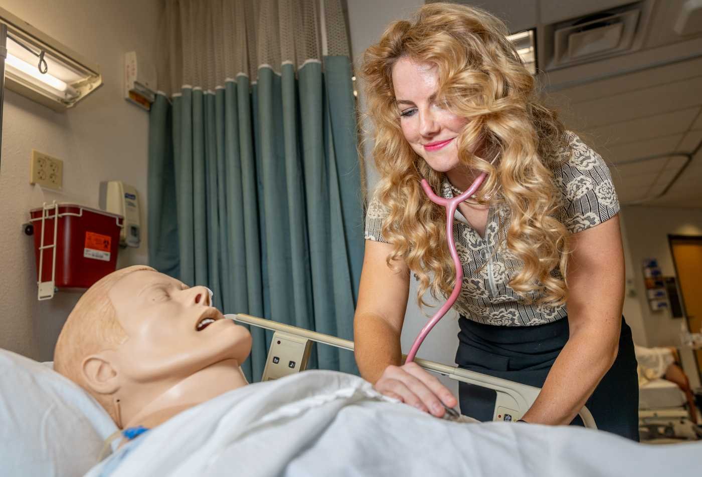 A graduate student practices patient assessment using a patient simulator, showcasing hands-on learning in the Health Care Simulation, MS.