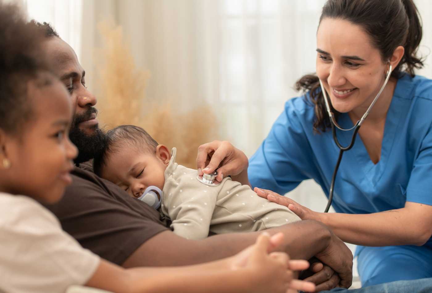A nurse practitioner performs a health assessment for an infant while discussing care with the child's family, representing the field explored in the Primary Care Pediatric Nurse Practitioner (Graduate Certificate).