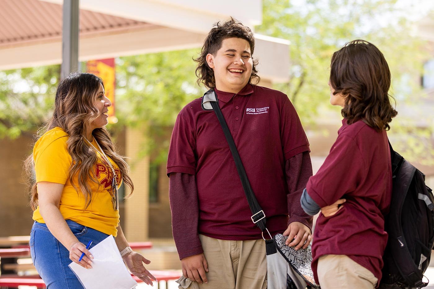 Three students in maroon and gold shirts chat outdoors on campus, capturing the welcoming spirit of ASU's Youth Services Leadership program.