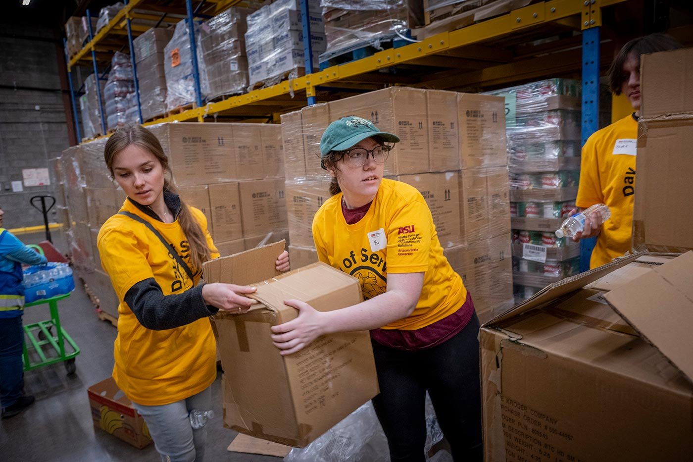 Two students in gold shirts pack supply boxes in a warehouse, reflecting the service focus of ASU's Community Resources and Development degree.