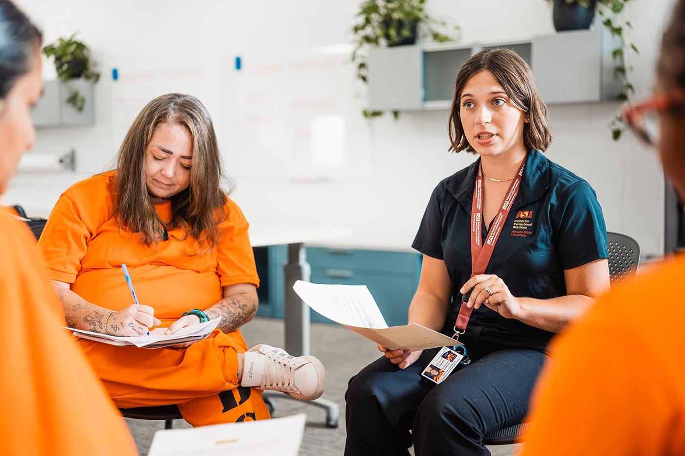 An ASU student leads a discussion with women in orange jumpsuits, focusing on the rehabilitation work central to this degree.
